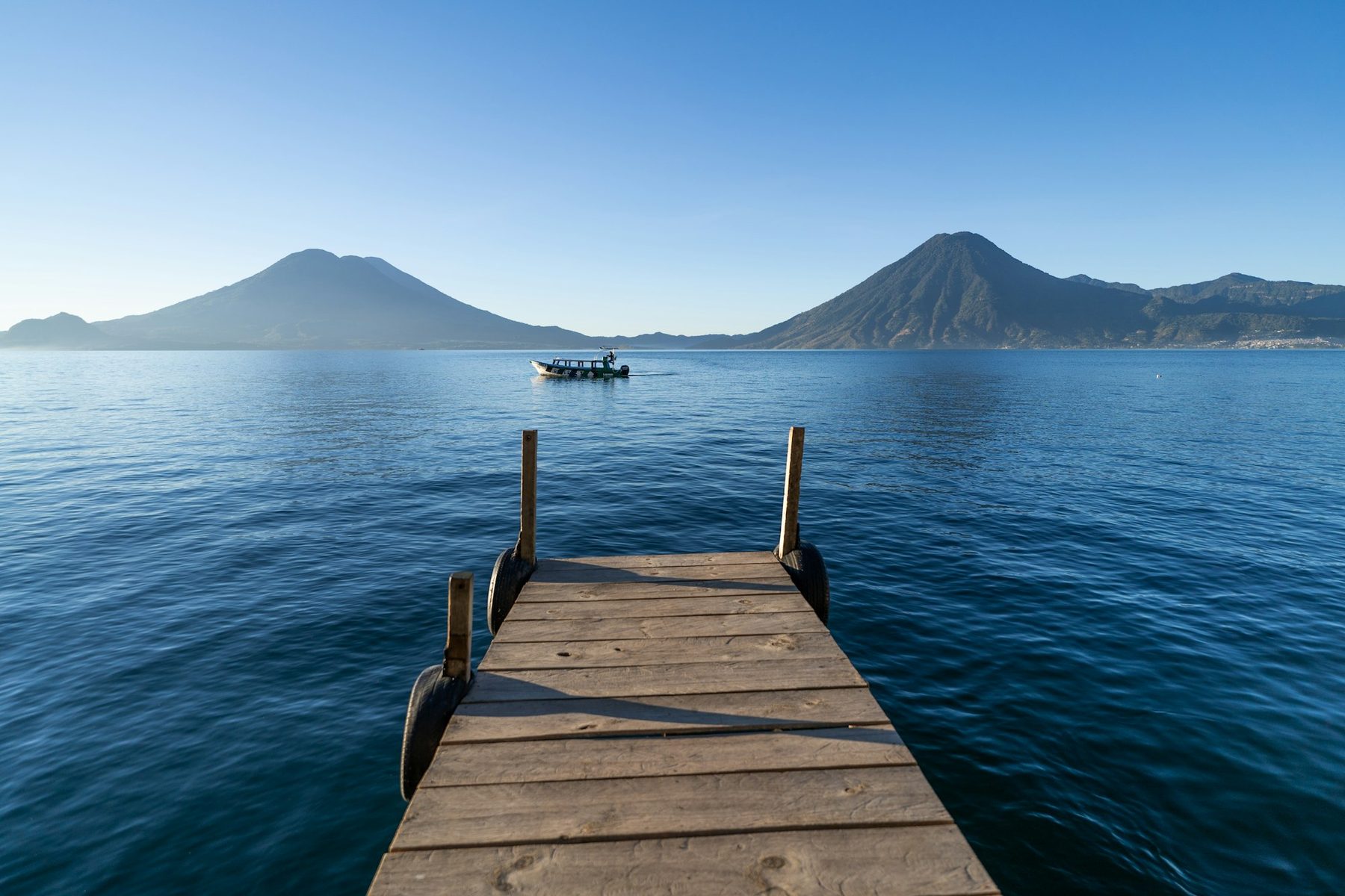 A wooden dock reaching into Lake Atitlan with volcanoes across the water