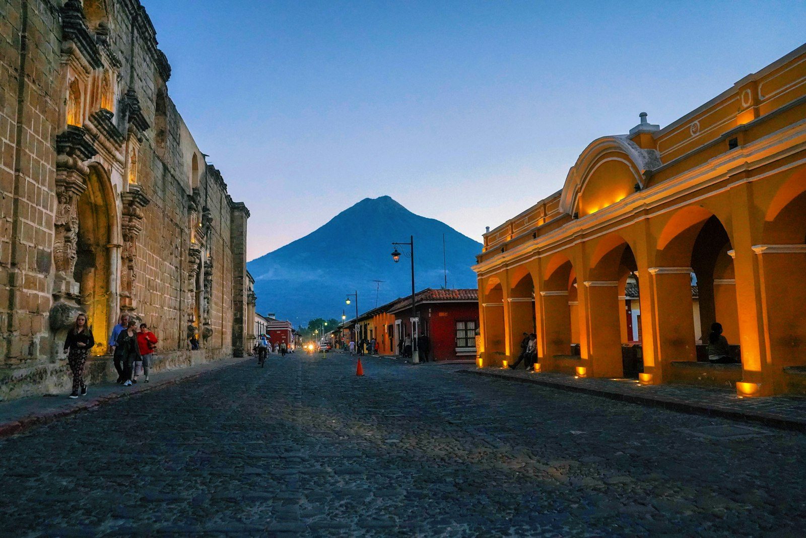A cobblestone street in Antigua Guatemala at dusk with Volcan de Agua behind