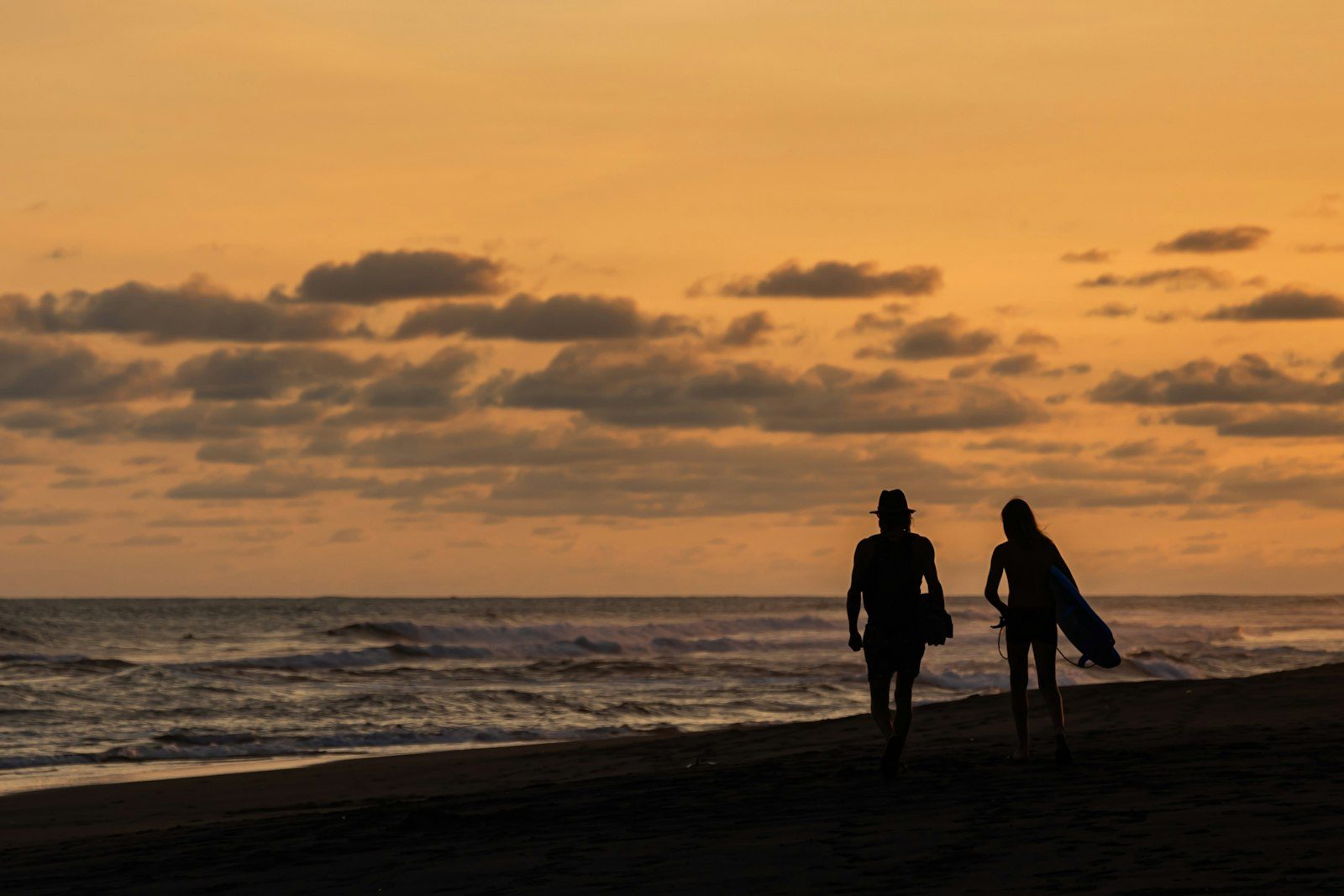 Surfers on the black sand beach at El Paredon at sunset